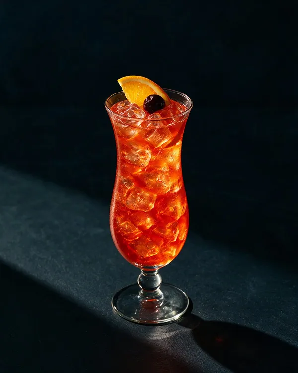 Klarröd Hurricane i ett orkanformat glas med is, apelsinskiva och rött cocktailbär