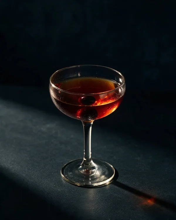 Mörkröd Manhattan i kyld coupe med ett mörkt cocktailbär i botten