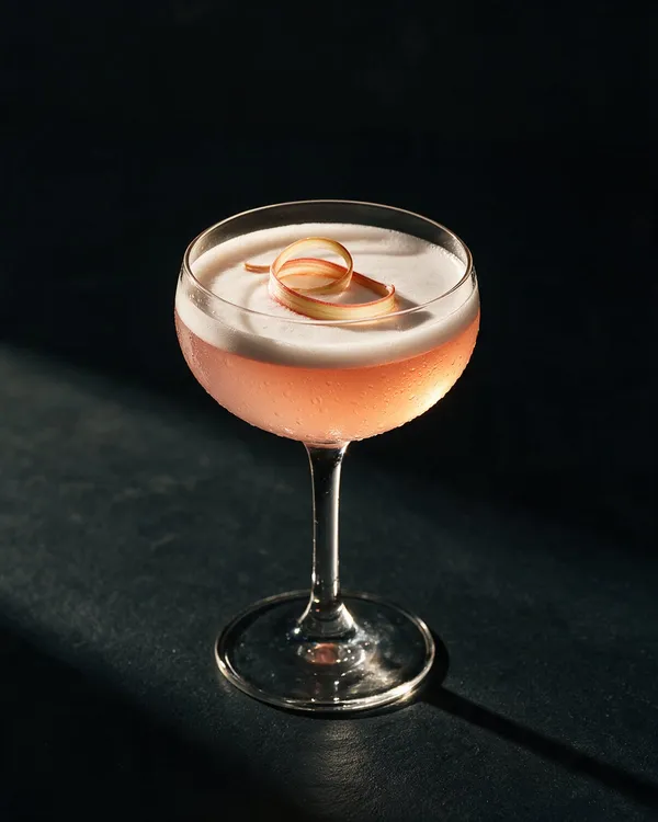 Rosa Rabarber Sour i coupeglas med vitt skum och en tunn rabarberremsa