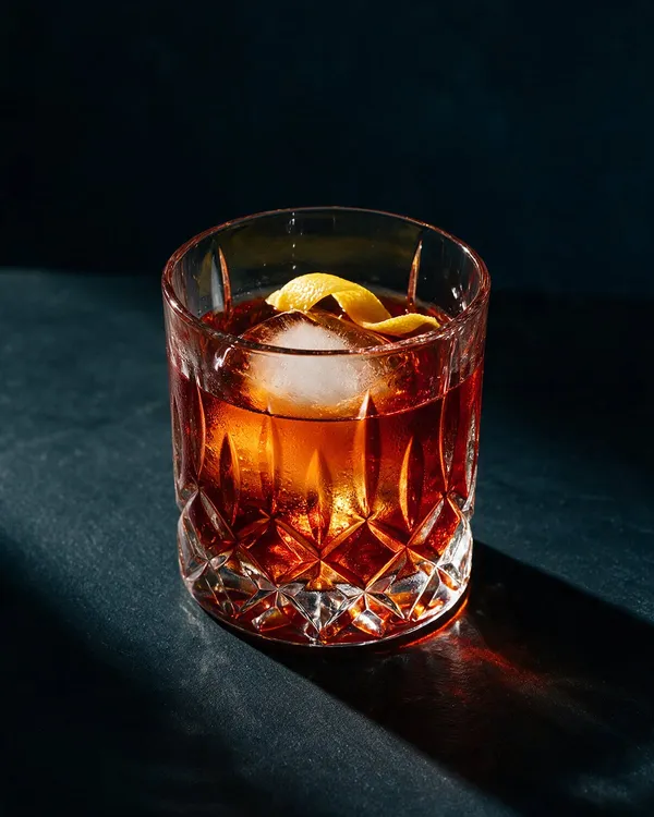 Mörk bärnstensfärgad Vieux Carré i rocksglas med stor isbit och citronzest